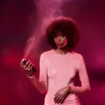 Woman with voluminous curly hair spraying Oudgasm Rose Oud | 16 Hair Mist