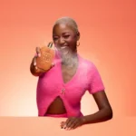Woman in a pink top holding an Eden Sweet Peach | 35 Kayali Eau de Parfum bottle