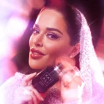 Woman holding a small black Rose Oud bottle near her face