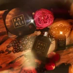 Café Oud bakhoor jar with two perfume bottles, coffee beans and a pink rose on oud wood