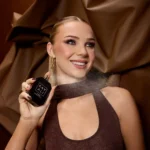 Woman spraying Oudgasm Chocolate Oud near her neck against a brown satin backdrop