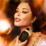 Woman holding a small black Vanilla Oud bottle near her face