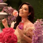 Woman holding a Fleur Majesty Rose Royale bottle near her face among red roses and pink flowers
