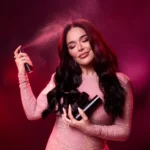 Woman spraying Oudgasm Rose Oud | 16 Hair Mist, holding several black Hair Mist cans