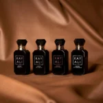 Four black Oudgasm miniature bottles standing in a row on bronze silk fabric
