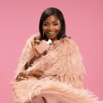 Woman in a pink feathery outfit holding a Yum Boujee Marshmallow | 81 bottle near her face