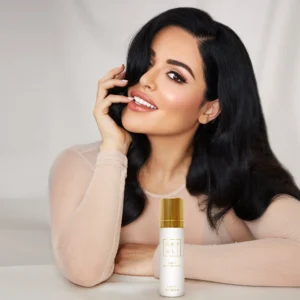 Woman with long dark hair holding a Déjà Vu White Flower | 57 Hair Mist bottle near her face