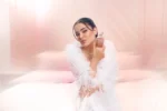 Woman in a white feathered outfit seated in a Musk | 12 Kayali campaign photo