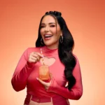 Woman in pink holding an Eden Sweet Peach | 35 Kayali Eau de Parfum bottle