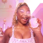 Woman with curly blonde hair in a pink top holding a Vanilla Candy Rock Sugar | 42 bottle near her face