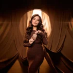 Woman in a brown dress holding a Freedom Musk Matcha | 45 bottle against draped fabric
