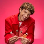 Man in a red jacket holding the four Eden Obsessions miniatures against a pink background