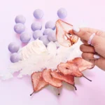 Hand holding a Vanilla Candy Rock Sugar | 42 bottle over purple candies, rock sugar crystals and dried orange slices